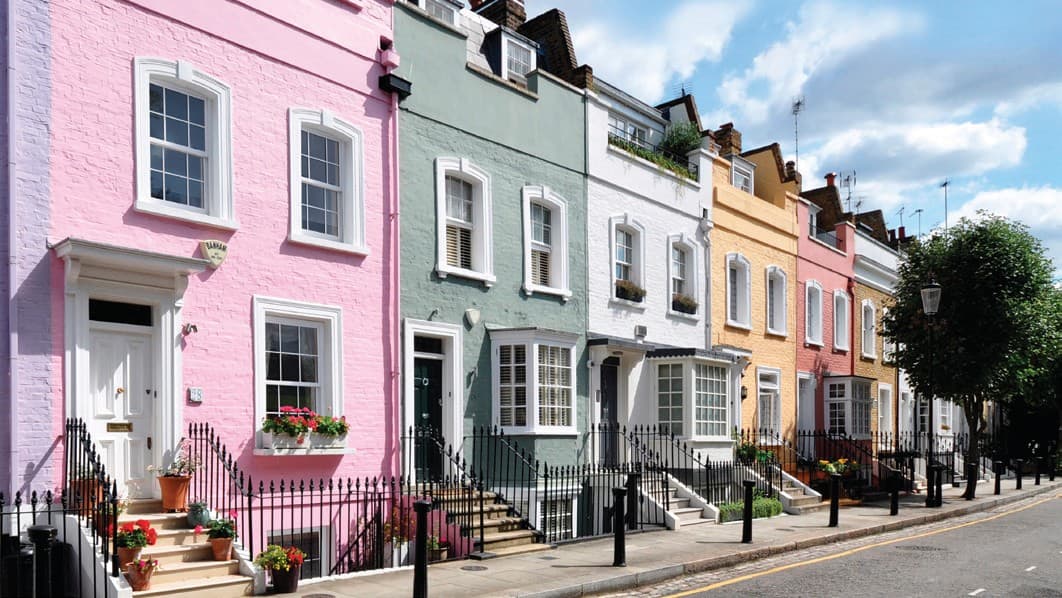 A painted London terrace with sliding sash windows throughout, iron railings and a blue sky
